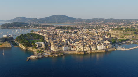 Old Town of Corfu and harbor lit by sunrise with calm sea and pastel skies above, panoramic stunning establish overview