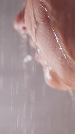 happy woman with water pouring on face in bathroom closeup. smiling lady takes relaxing shower in home washroom. reducing stress with spa care