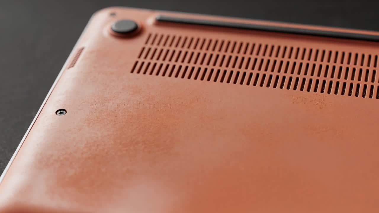 Panning camera from close showing orange laptop base vents screw foot on black table for inspection