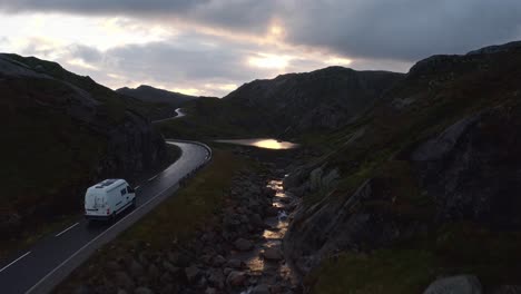 winding road through the norwegian mountains, a camper van passing at sunset