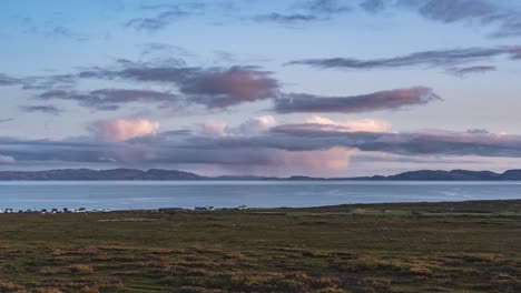 nubes grises iluminadas de rosa por el sol poniente sobre el fiordo de vardo y la tundra de otoño