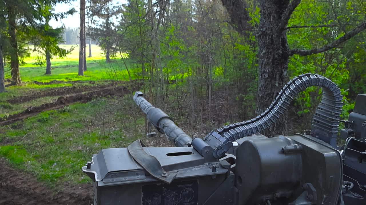 Rare footage panning over an armed cannon or a gun on top of a British army Challenger 2 4034 tank during a summer sunny day in a forest where it is hinnden behind braches and twigs. Bulletbelt seen.