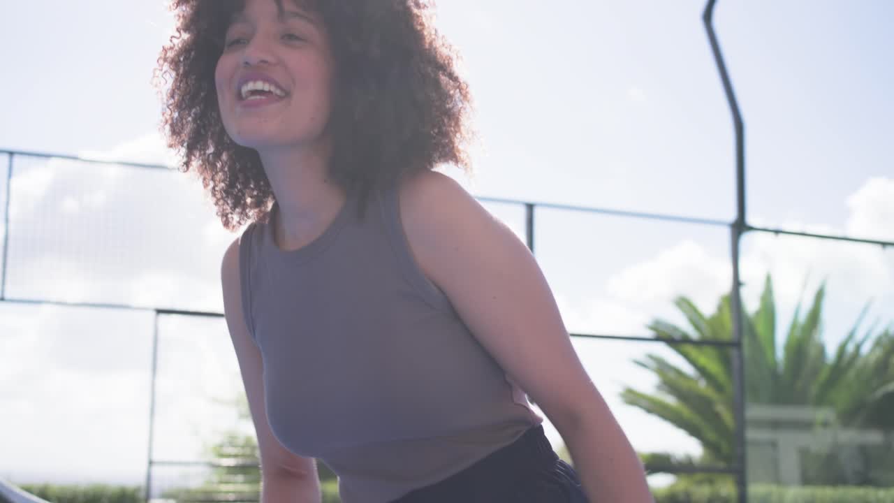 Mulher afro-americana apertando as mãos na rede, trocando raquete, bolsa e garrafa de água enquanto se afasta