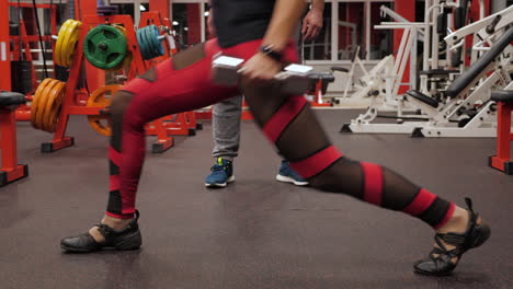 a woman doing leg lunge with weights in a gym under the supervision of a coach