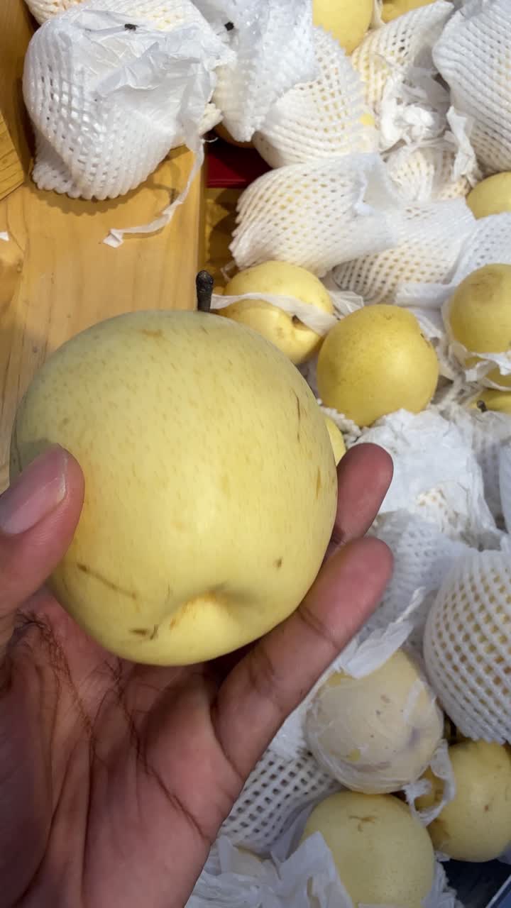 Mano che tiene e ruota una pera gialla fresca in un mercato.