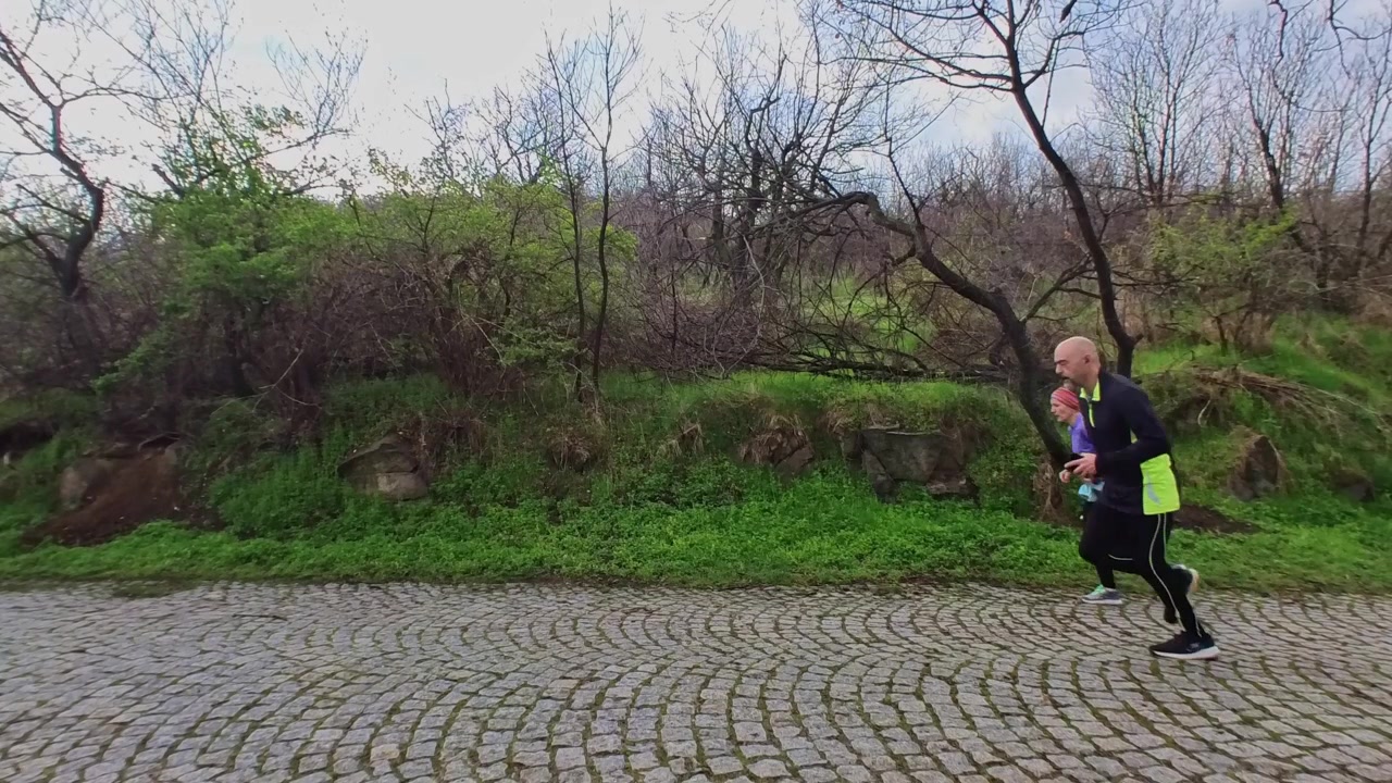 Casal ativo correndo junto ao longo de um caminho de paralelepípedos na colina da juventude em Plovdiv, Bulgária, cercado por árvores e vegetação durante um treino ao ar livre