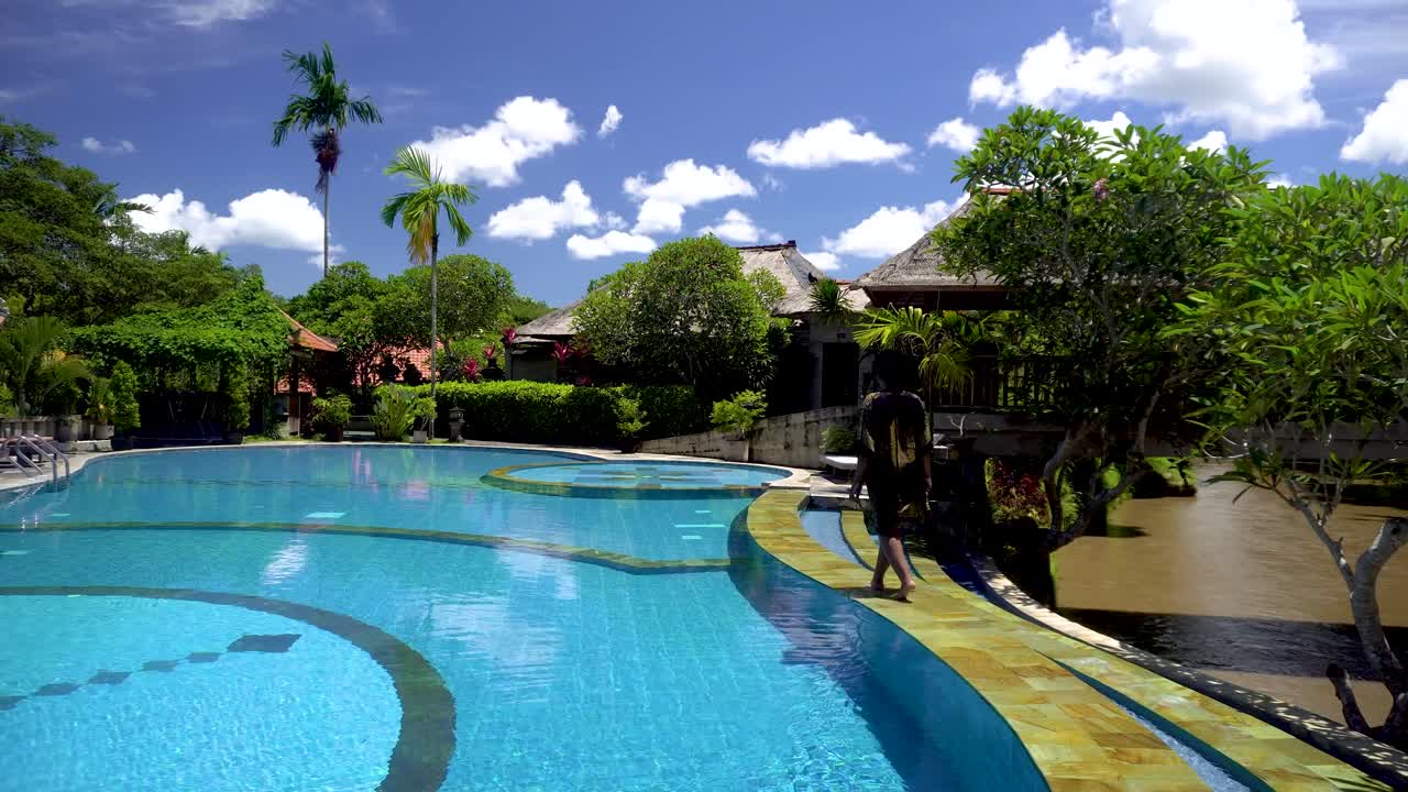 African American woman walking along the pool at the luxury hotel during a bright sunny day. she has a big afro and wears a robe