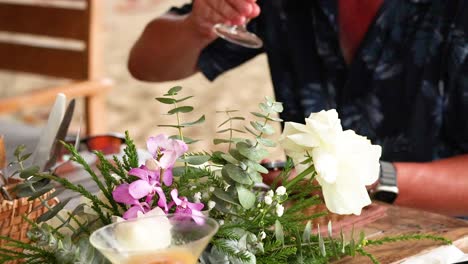 a person prepares a cocktail amidst vibrant flowers on a sunny beach in phuket, thailand. natural lighting enhances the tropical ambiance