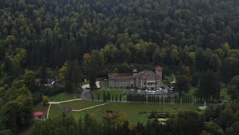 Aerial-view-of-a-big-palace-and-its-gardens-between-mountain-trees-on-a-clouded-day
