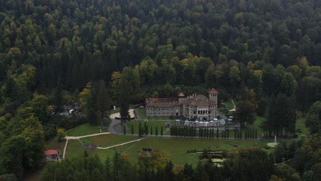 aerial view of a big palace and its gardens between mountain trees on a clouded day