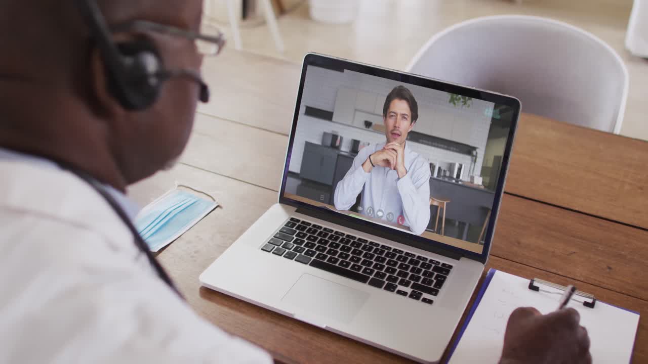 Afroamerikanischer Geschäftsmann sitzt am Schreibtisch und führt per Laptop einen Videoanruf mit einem männlichen Kollegen.
