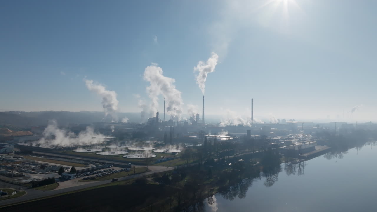 Ampia veduta aerea della cartiera di Štětí con più ciminiere che emettono vapore, infrastrutture industriali e il corridoio fluviale visibile attraverso una tenue foschia atmosferica.