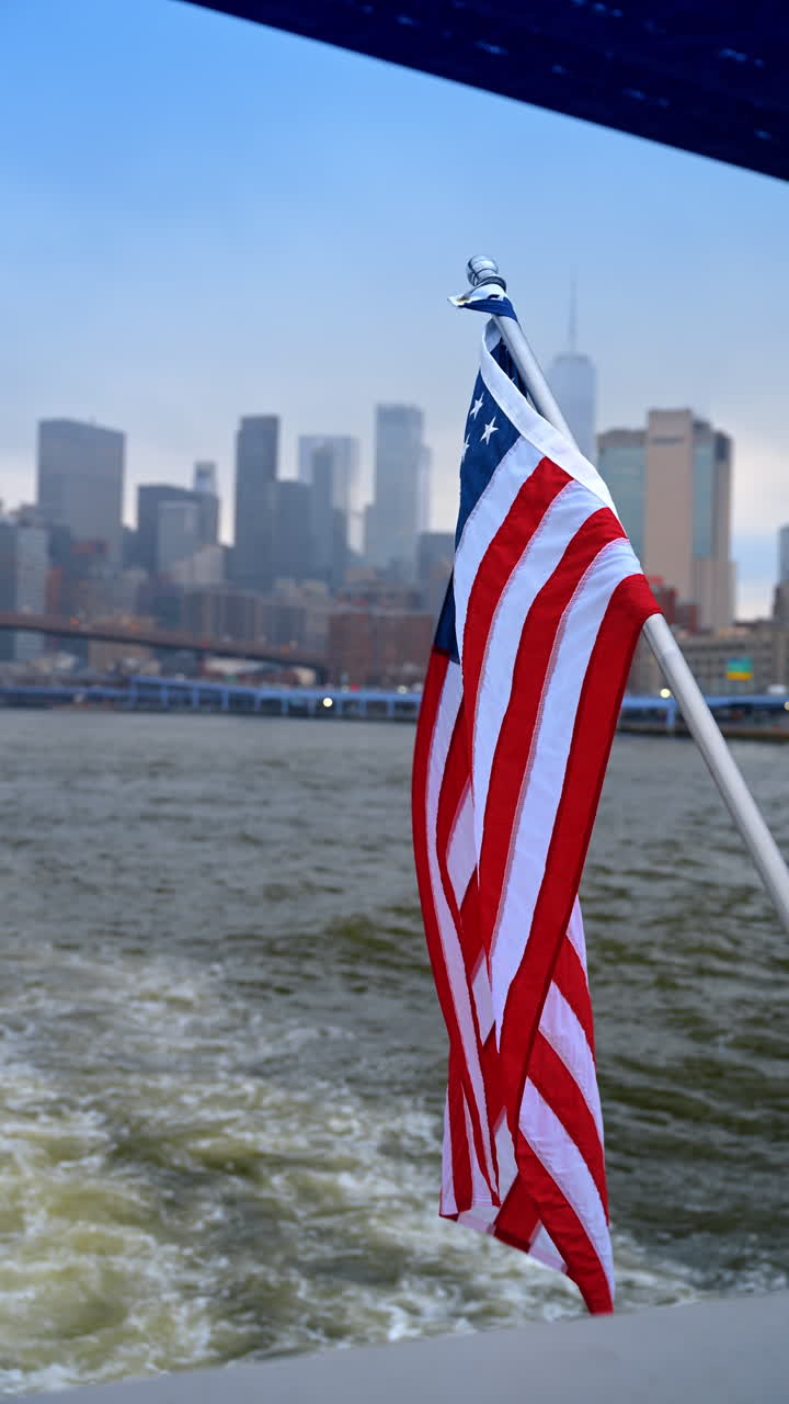 Bandiera americana che sventola su una barca con lo skyline di New York sullo sfondo. Primo piano della bandiera statunitense su una barca con lo skyline sfocato di Lower Manhattan in lontananza.