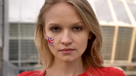 portrait of a young blonde girl soccer fan of england looking into the camera, serious face, stadium in the background 50 fps