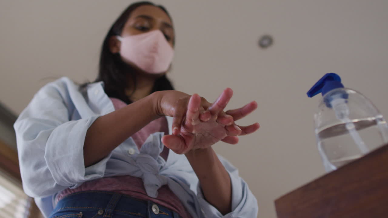 Mixed race woman wearing mask at home disinfecting hands