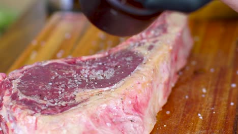 chef condimentando un filete jugoso en el hueso arrojando sal y pimienta sobre él, preparación de carne en cámara lenta de primer plano