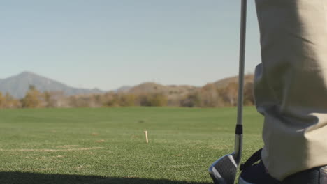 Close-up-of-golf-ball-being-hit-with-driver-while-younger-son's-legs-stand-in-foreground