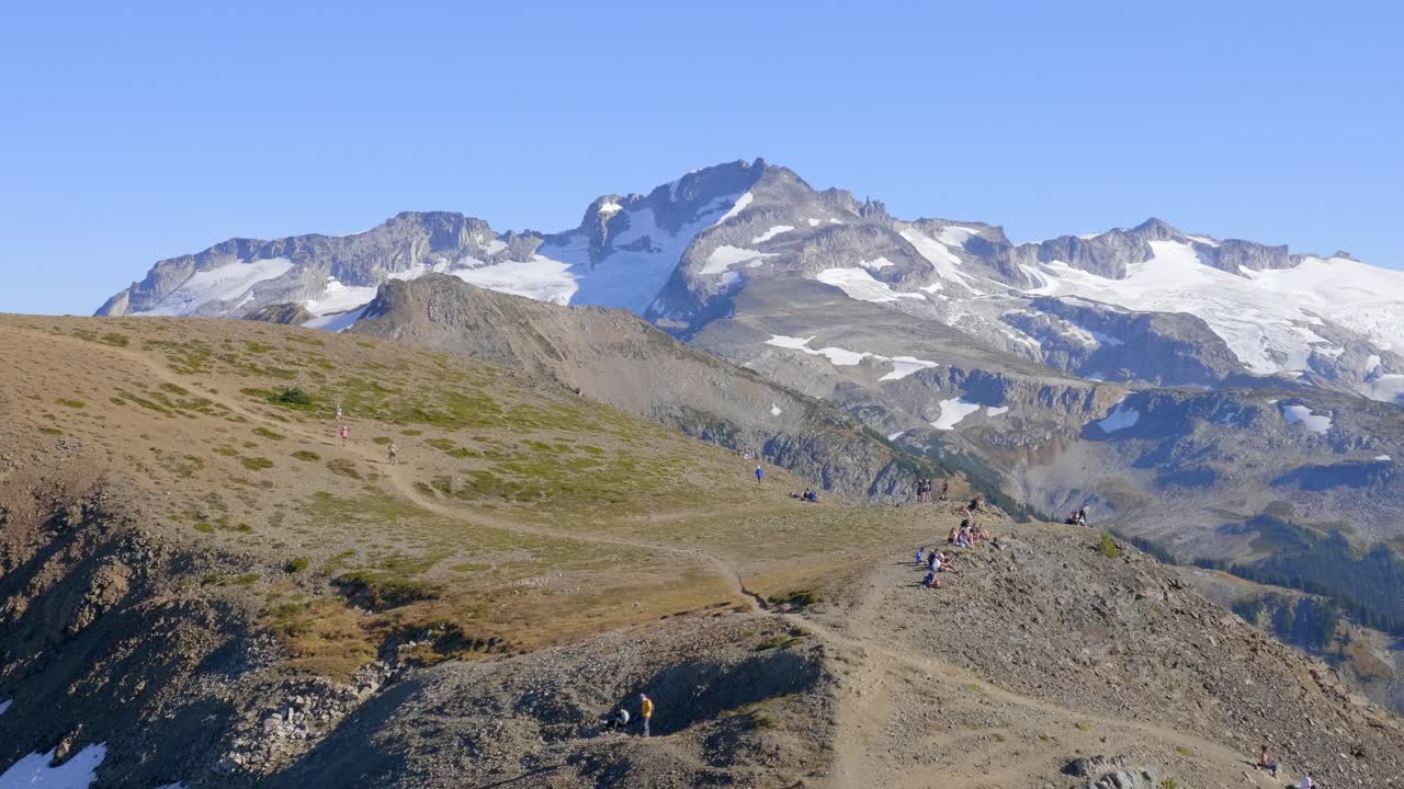 excursionistas en la ruta de senderismo en un día soleado en whistler, columbia británica, canadá con montaña nevada y fondo de cielo azul