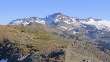 hikers on the hiking trail on a sunny day in whistler, british columbia, canada with snowy mountain and blue sky background