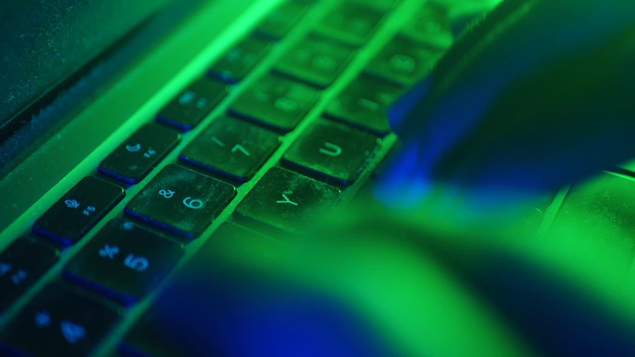Close-up of hands typing on a laptop keyboard in neon light