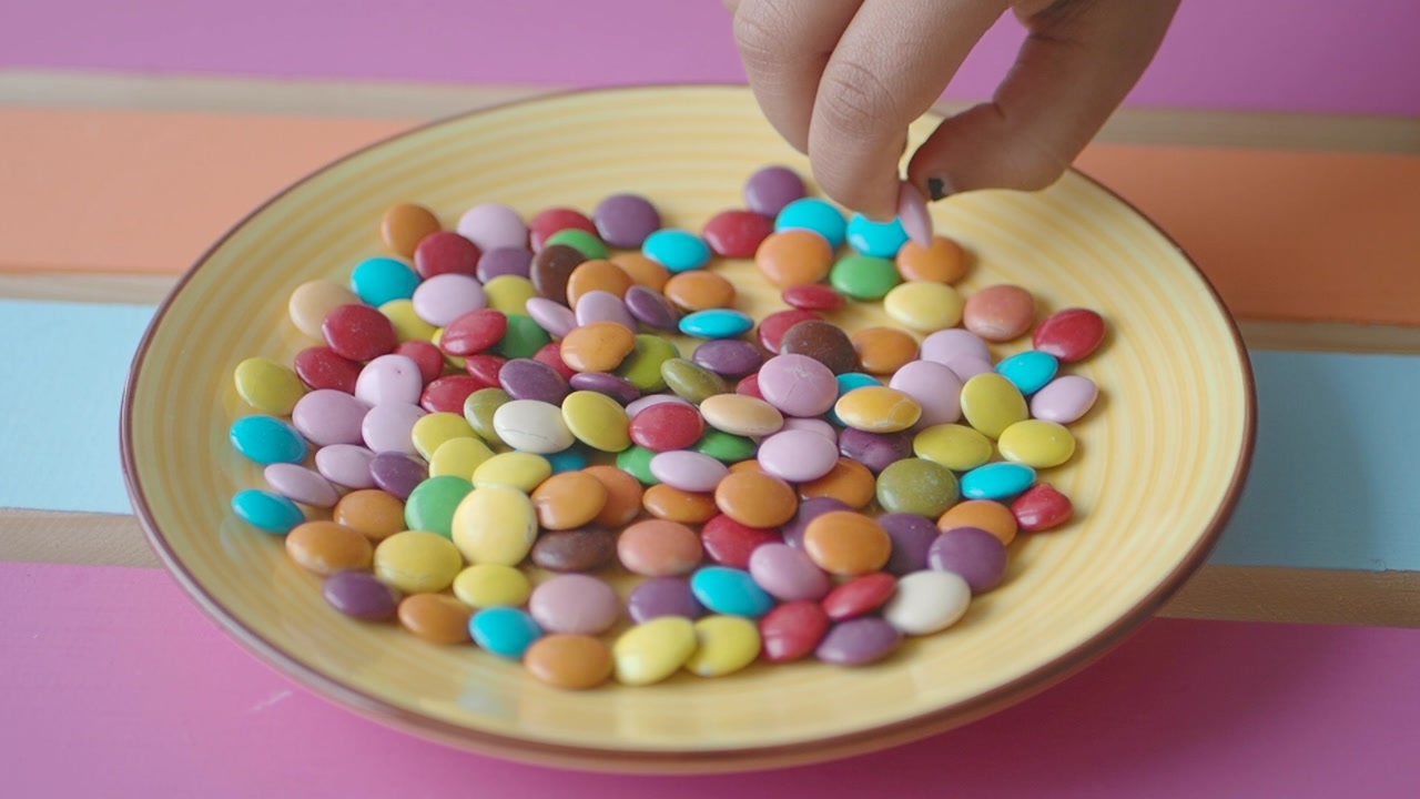 Hand Picking a Colorful Candy from a Yellow Plate