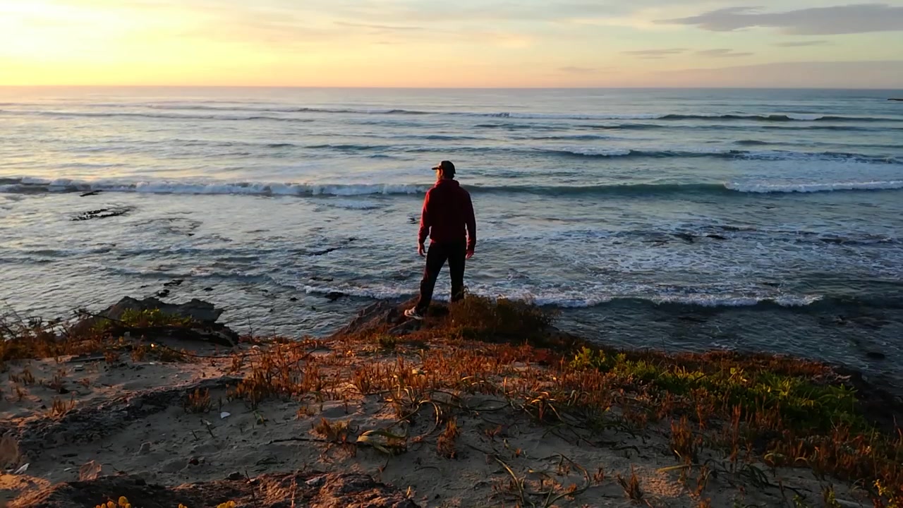 Viaggiatore avventuroso che cammina verso il bordo di una scogliera sul mare all'alba.
