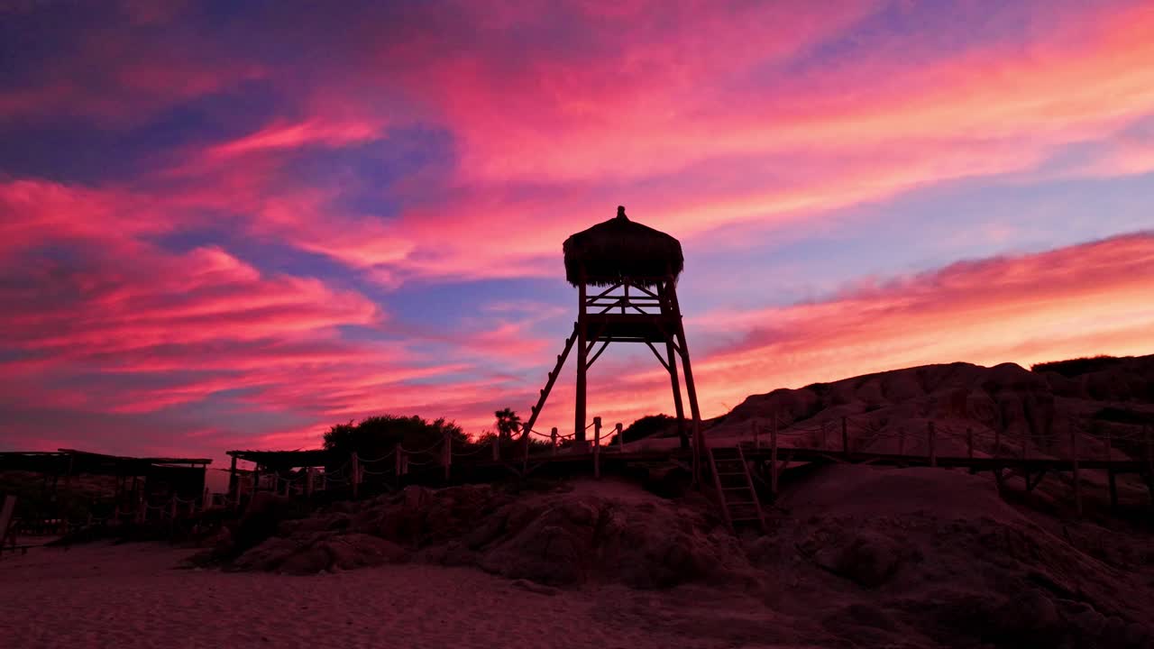 silueta de salvavidas de madera en una playa tropical con nubes rojas rosadas al atardecer, cabo pulmo