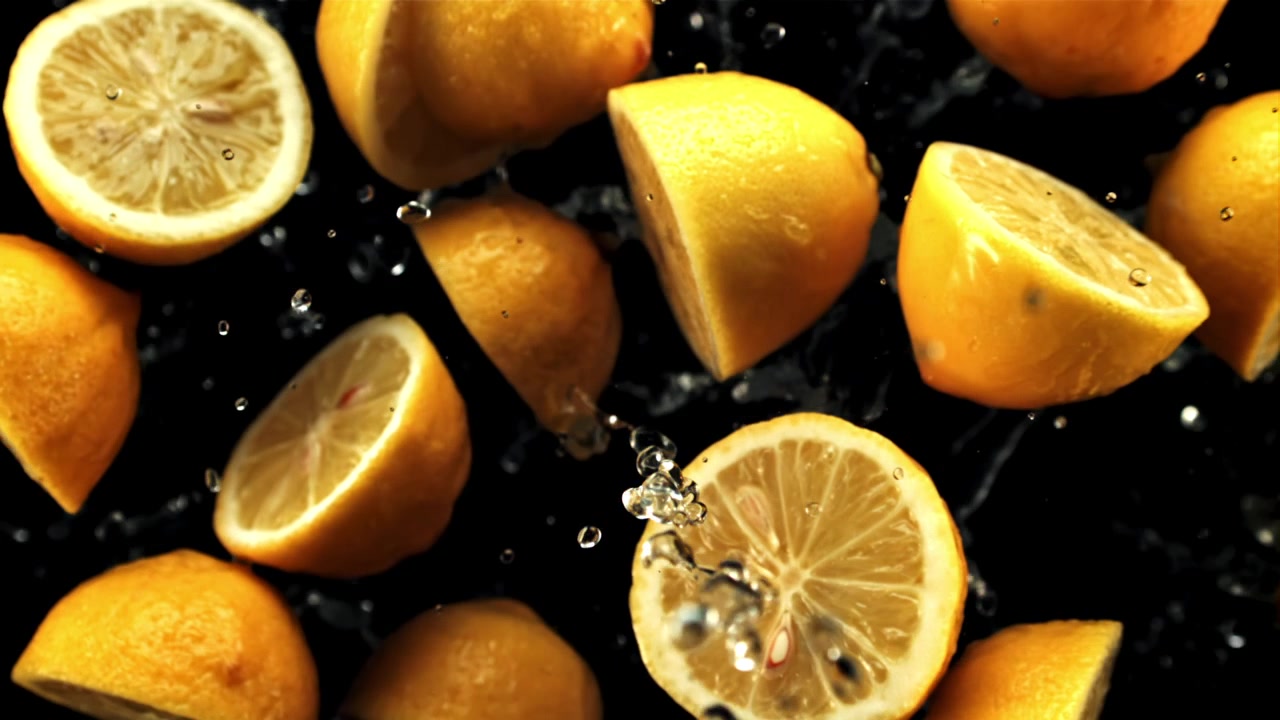 Limoni gialli freschi e metà con schizzi d'acqua su sfondo nero