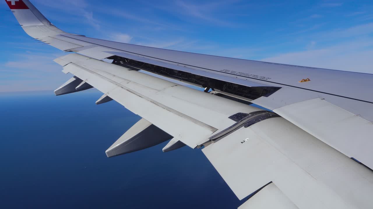 View from an airplane window showing the wing and moving flaps above the Atlantic Ocean near Lisbon Portugal during a sunny landing approach. Travel and aviation concept