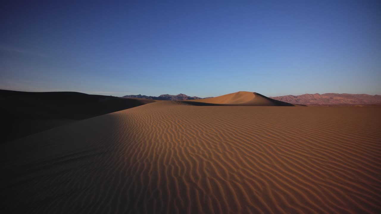 Wide view of the sand dunes in the Grand Canyon desert, showcasing the textured sand patterns under the clear blue sky. A serene and vast landscape of the American desert