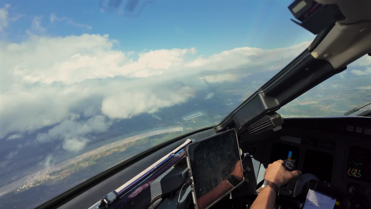 An immersive cockpit view. Hand of a caucasian pilot grasping the flight controls insde a jet cockpit while flying through a blue sky with few stratus clouds.