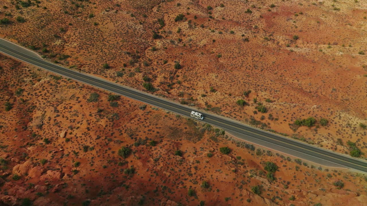 White trailer going by the road in the deserted land of Utah, USA. Drone footage over the sandy land and rounded rocks of canyons. Atop view.