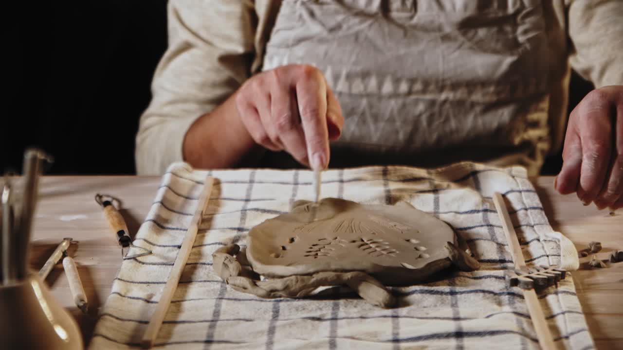 una joven alfarera hace patrones en la pieza de arcilla usando una herramienta