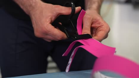 person cutting pink athletic tape with scissors