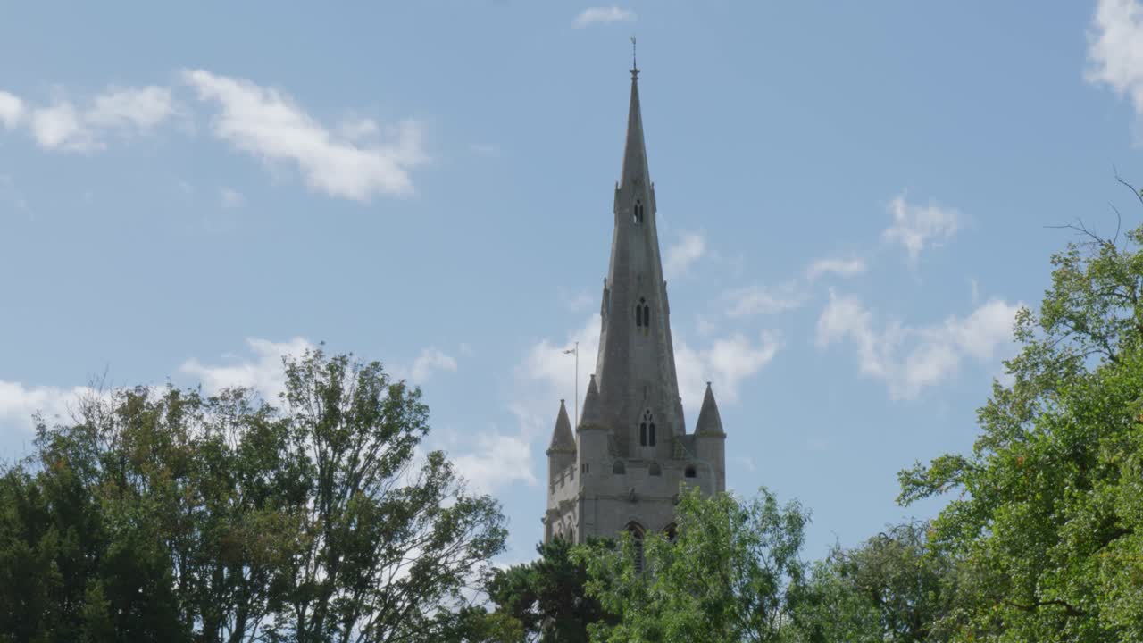 Tall spire in Oakham against blue sky and trees, peaceful and historic