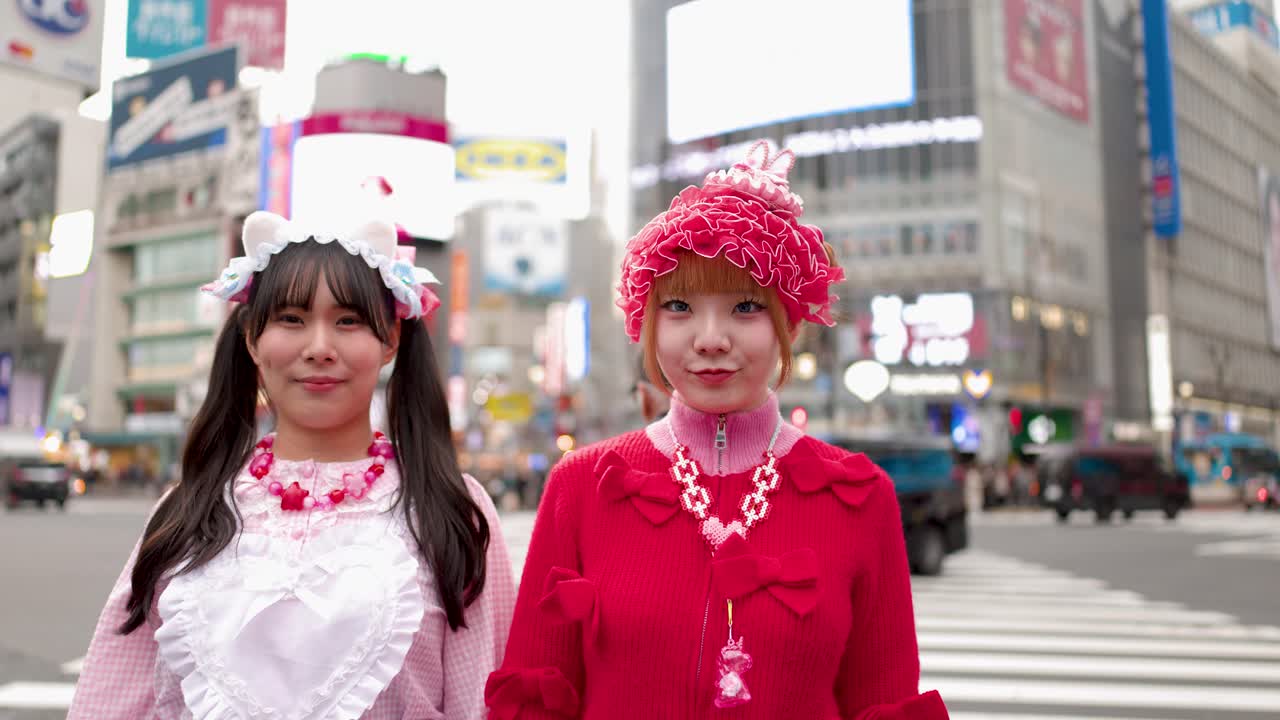 Due donne con vivaci abiti rosa e rossi posano giocosamente a un trafficato incrocio di Tokyo.