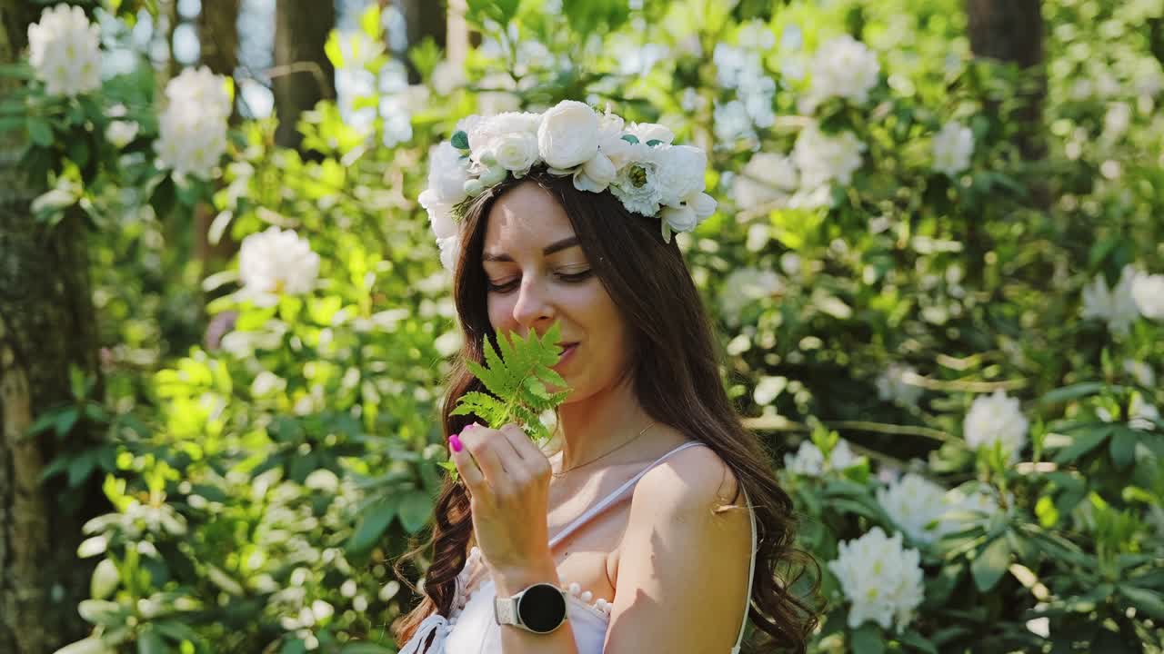 Slow motion medium shot of woman smelling fern among white rhododendrons