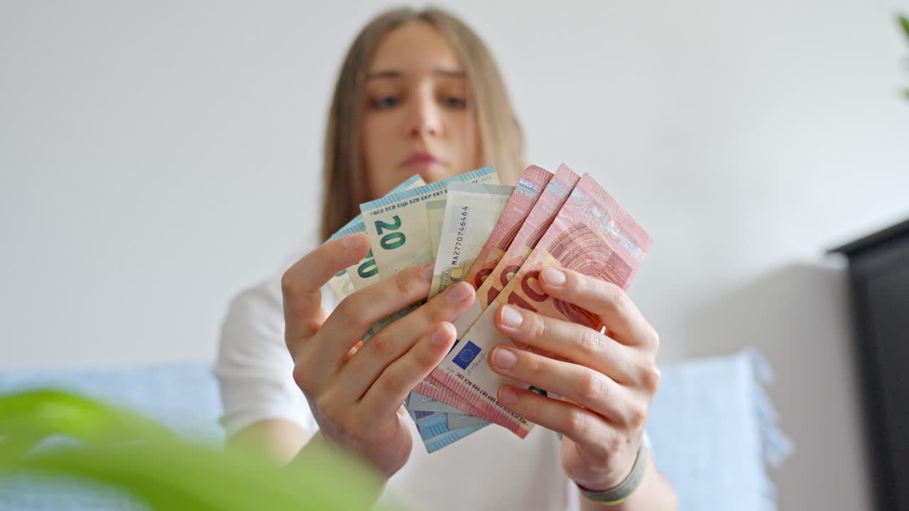 mujer con billetes en efectivo en euros en sus manos hacia la cámara en casa mientras los mira fijamente, estático