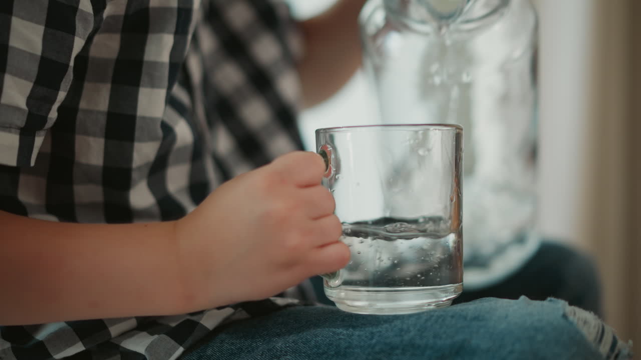 Child pouring water into a glass cup