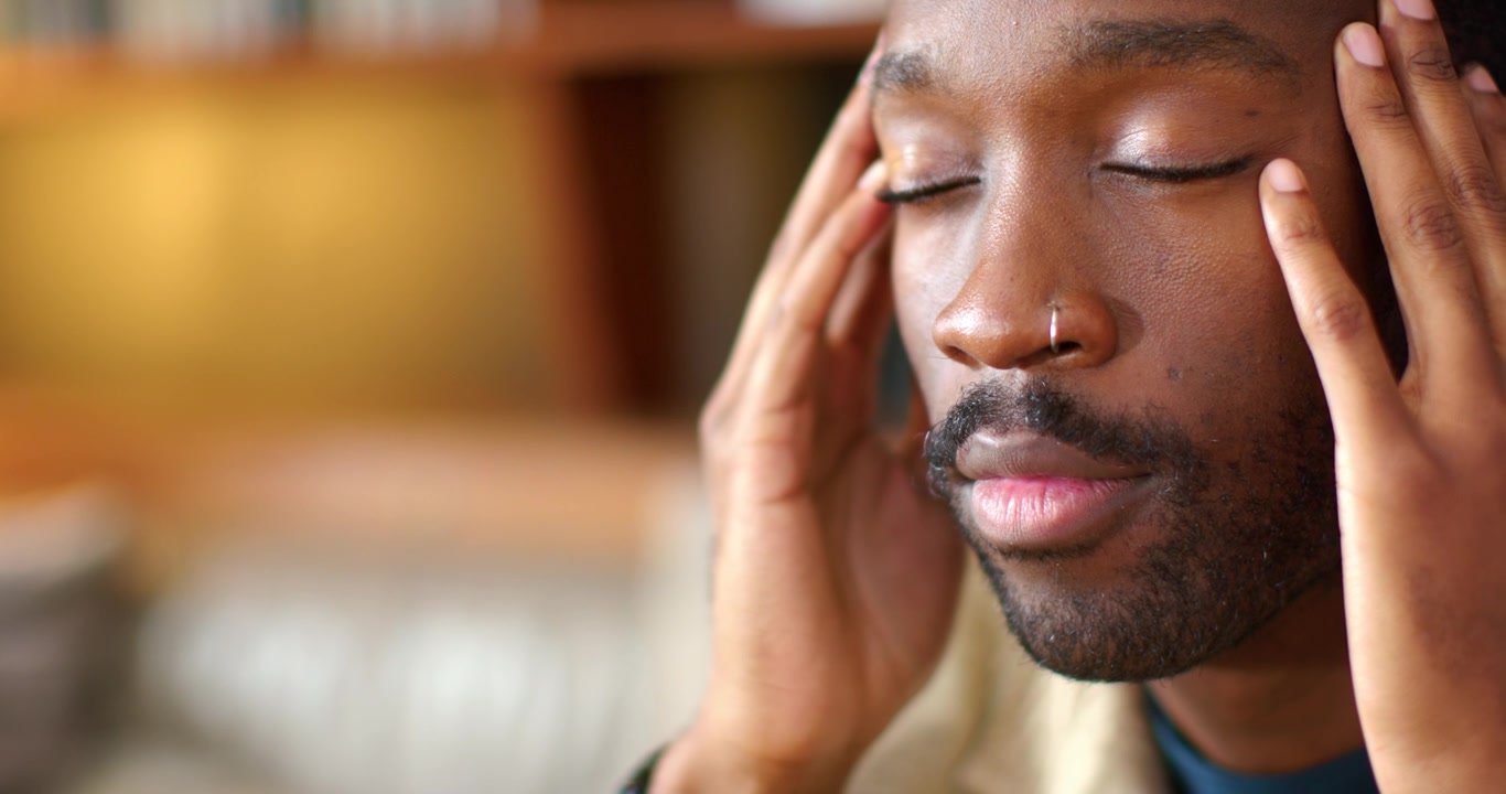 African American man feeling tension, pressing temples and rubbing forehead on couch, nose ring