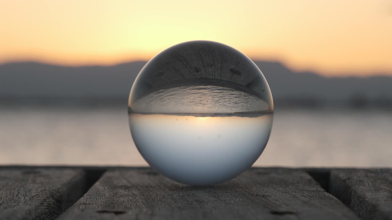 해가 지는 동안 크리스탈 공에 해변의 거울이 거꾸로 반사됩니다.