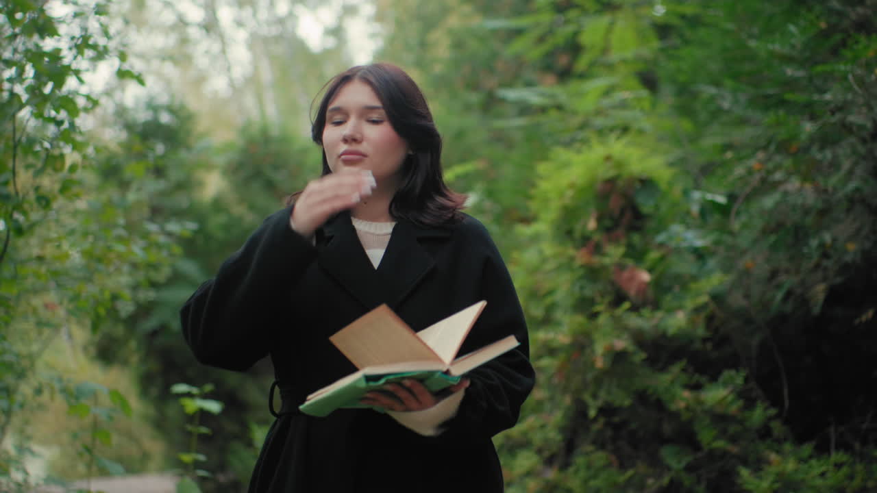 숲 속에서 책 페이지를 넘기며 산책하는 평온한 사람, 주위를 둘러보고 조용한 가을의 초록빛을 즐기며 부드러운 햇살과 바스락거리는 나뭇잎 소리를 듣고 마음 챙김 무드로 독서와 자연 속으로 천천히 빠져드는 모습이에요.