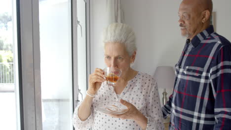 happy senior biracial couple drinking tea and embracing at home, slow motion