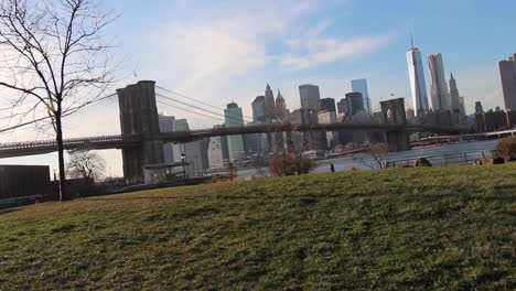 Puente-De-Brooklyn,-Torre-De-La-Libertad-Horizonte-De-Manhattan,-Plano-General,-Autos-Y-Mujer-Paseando-A-Un-Perro