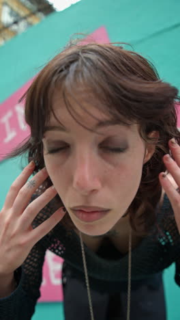 vertical video outdoor fashion portrait of young alternative style woman leaning in towards camera checking hair against graffitti covered walls of london city street uk in real time