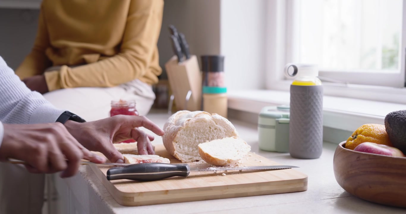 African family dad and teen, dad entering, spreading jam on bread for snack at kitchen counter