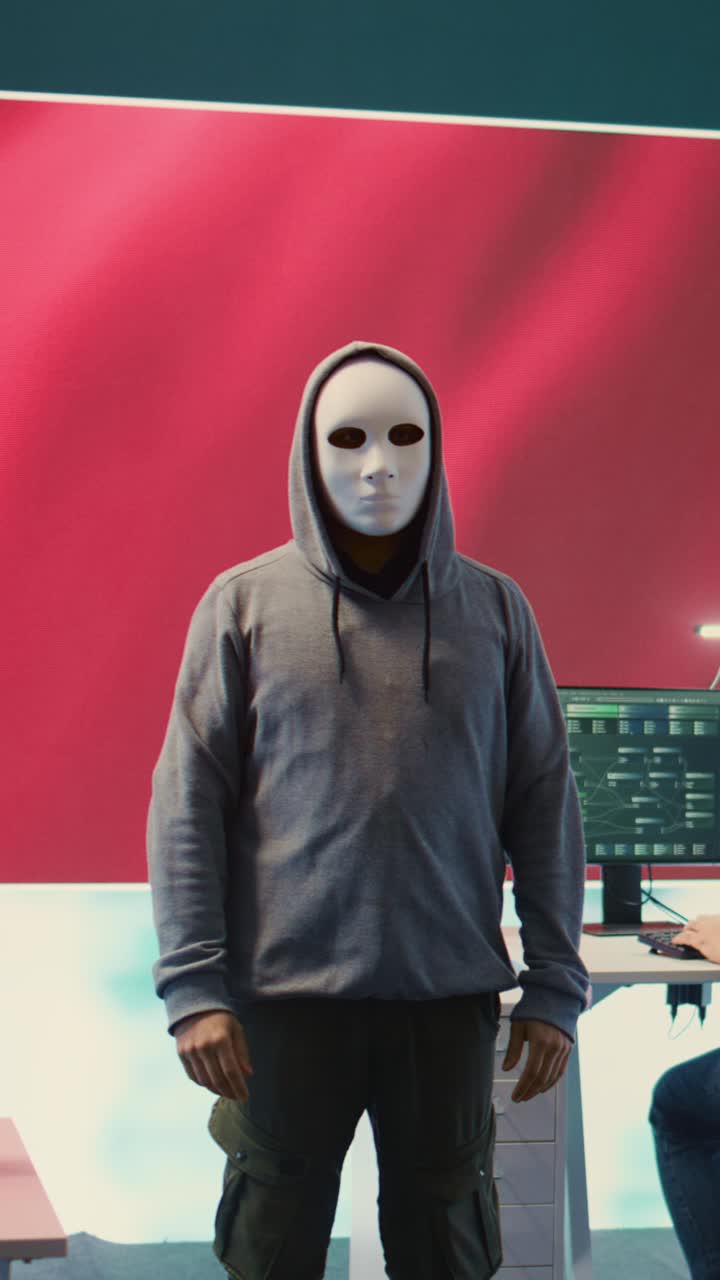 Masked Hacker in Hoodie Gesturing and Pointing at Computer Screen