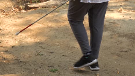 a blind woman walks with a cane through a natural area with a guide helping her explore the wilderness