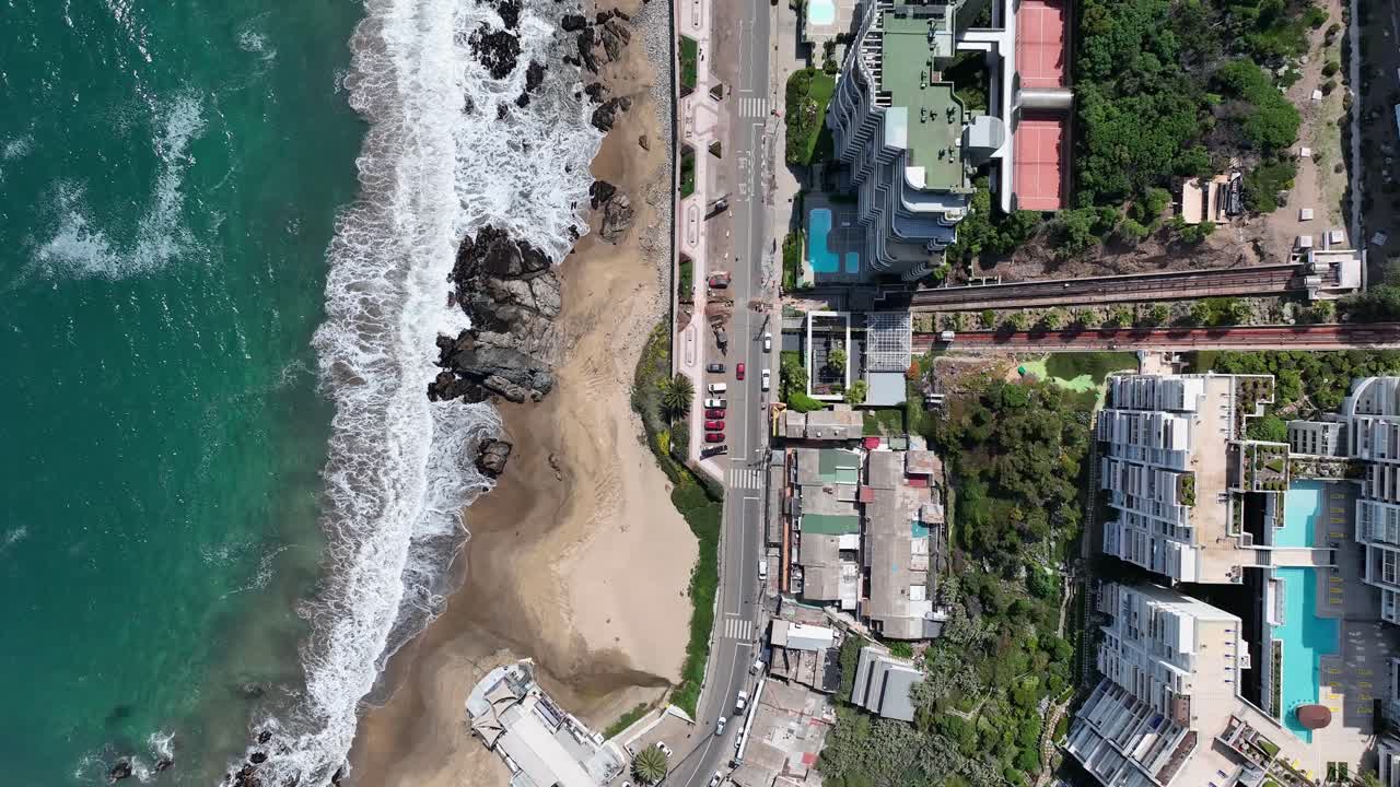 Top-down bird's eye drone view of Viña del Mar beach with turquoise waves, coastal highway, residential buildings, and swimming pools, Chile