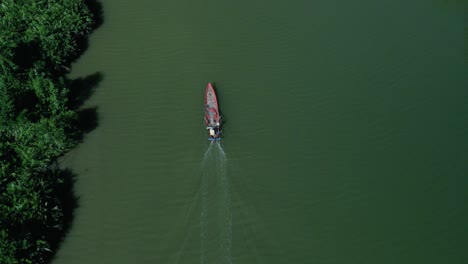 Simple-Asian-fishing-boat-traveling-along-clean-emerald-green-mangrove-coastline,-aerial-birds-eye-drone-view,-copy-space